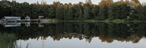 Vihreän luonnon ympäröimä Mytäjäisten uimaranta tyynenä kesäiltana. Taustalla radiomastot. Rannalla näkyvät laituri, hyppytori ja pukuhuone.
