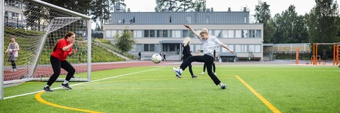 lapset potkimassa jalkapalloa tekonurmikentällä