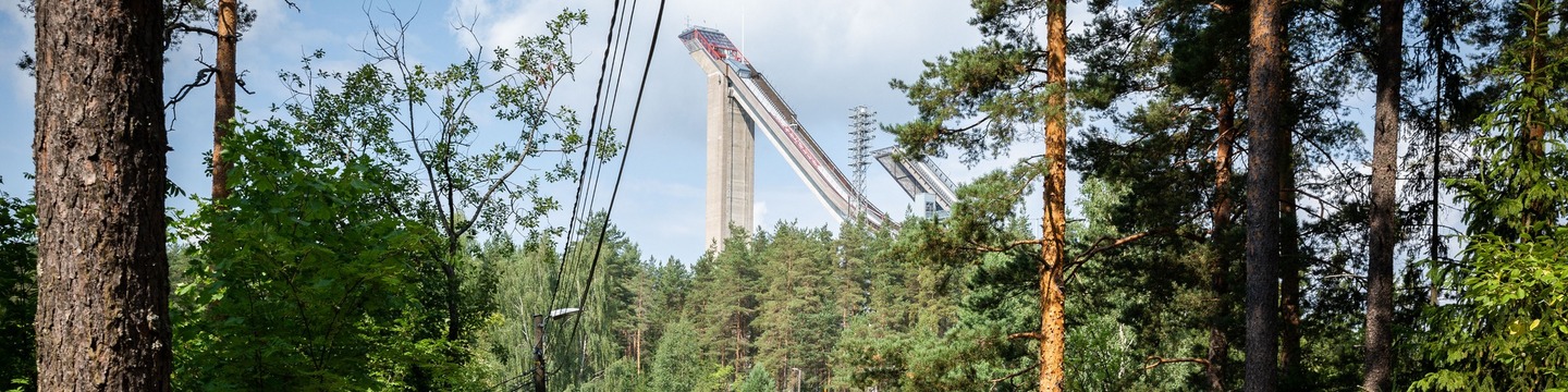 Kuvissa näkyy metsää ja puiden latvojen takaa näkyy Lahden hyppyrimäet