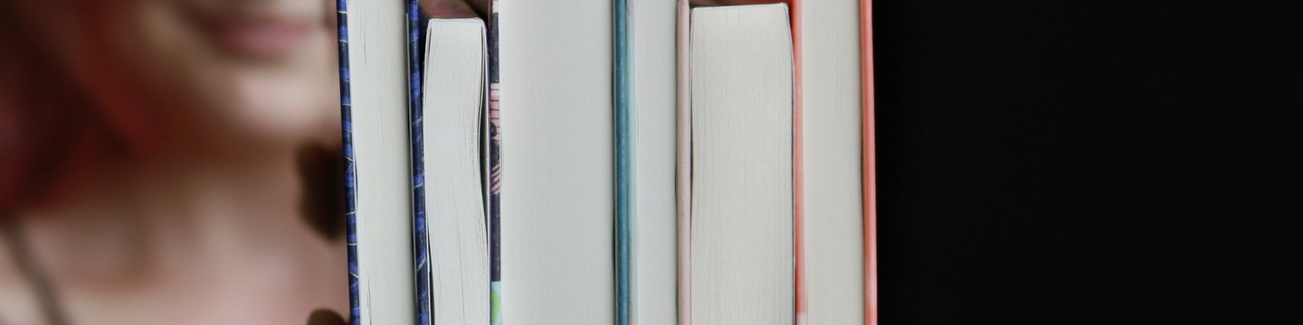 Nainen hymyilee ja pitää käsissään kirjapinoa 